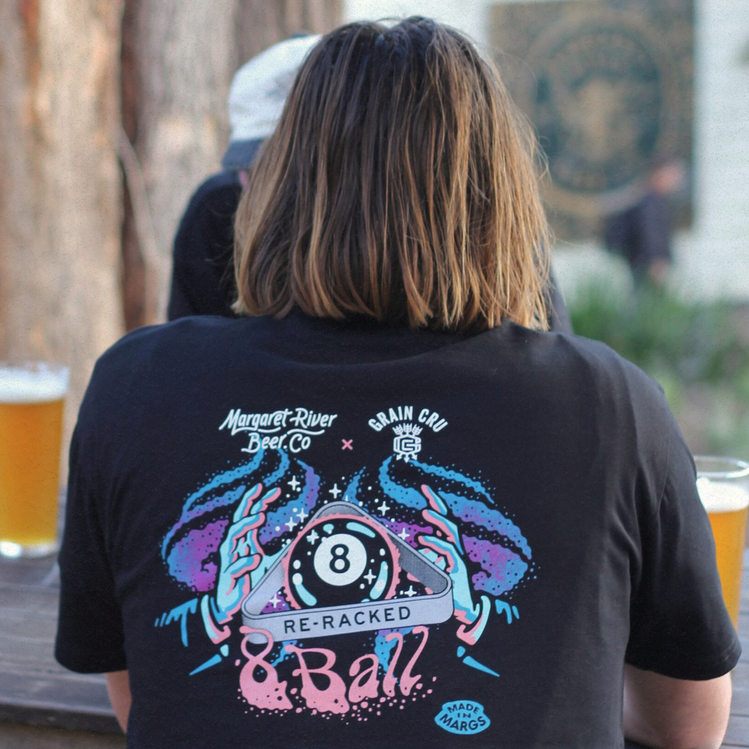 Person wearing a black t-shirt with a colorful design, sitting at an outdoor table with drinks.